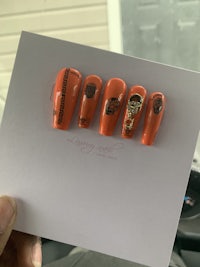 a person holding up a card with orange nails on it